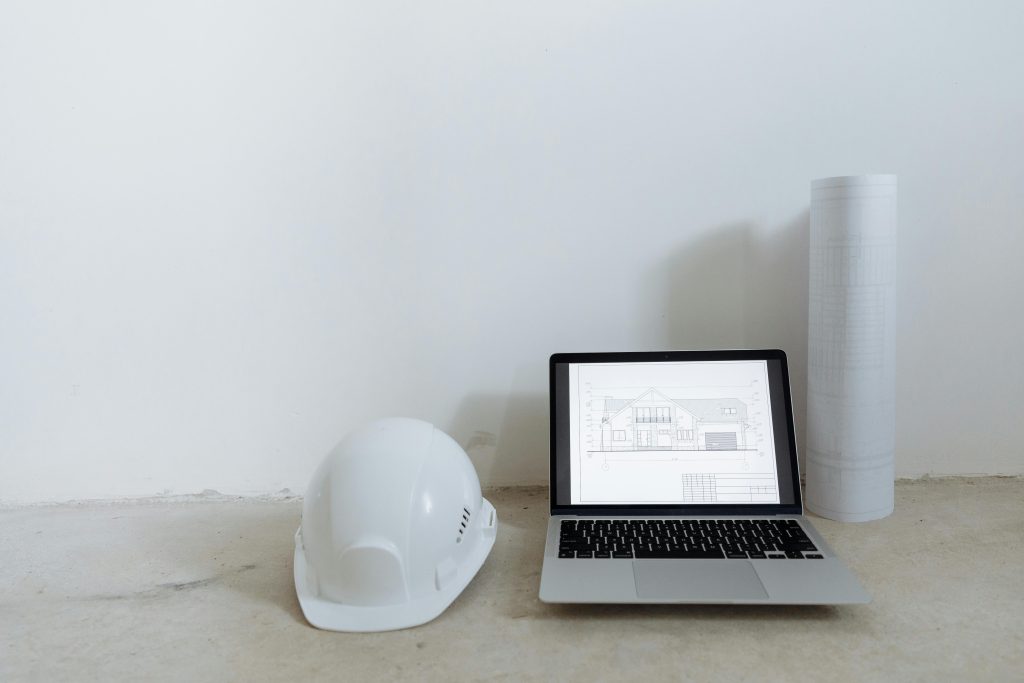 pexels-photo-8470809-8470809 A clean workspace with laptop, hard hat, and blueprints for construction planning.